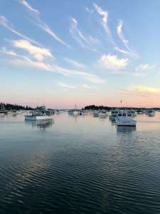 A pastel sunset near boats in the calm water. Women's counseling in Lynn, MA can be offered in person and online. Find support today with Aeon Counseling.